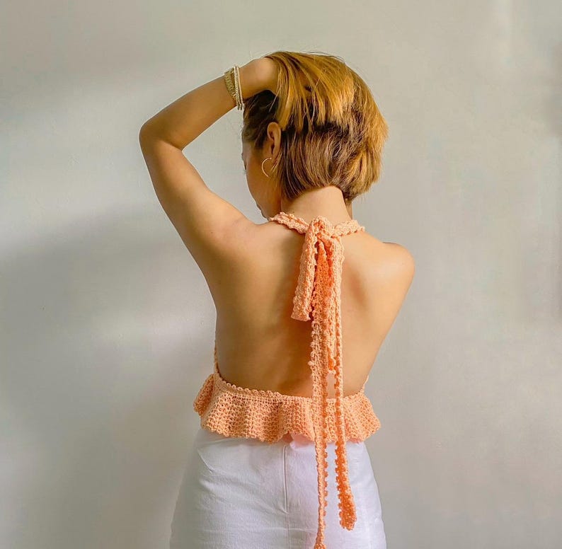 May include: A peach-colored crocheted halter top with a ruffled hem and a long tie in the back.