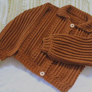 May include: A brown crocheted cardigan with a collar and button closure. The cardigan has a ribbed texture and is made with a chunky yarn.