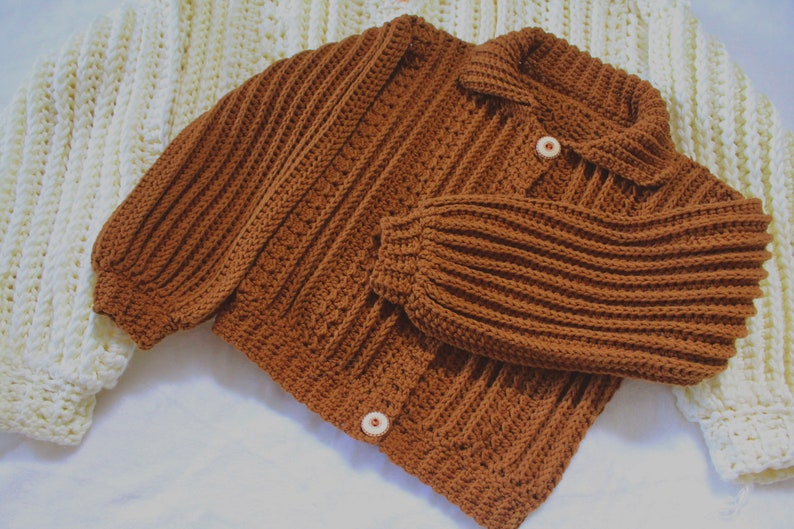 May include: A brown crocheted cardigan with a collar and button closure. The cardigan has a ribbed texture and is made with a chunky yarn.