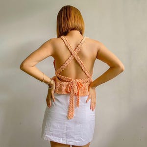 May include: A peach-colored crochet top with a criss-cross back design and a tie at the back.