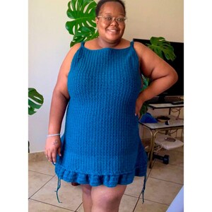 Puede incluir: Una mujer lleva un vestido de crochet azul turquesa con un dobladillo con volantes. El vestido tiene un escote cuadrado y es sin mangas.