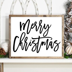 Może przedstawiać: Prostokątny drewniany znak z napisem "Merry Christmas" czarnym kursywą. Znak ma białe tło i brązową drewnianą ramę. Znak jest świąteczną dekoracją świąteczną.