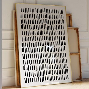 以下が含まれることがあります： 縦の線が幾何学的に並んだ白黒の抽象的なアートプリント。プリントは金色のフレームに収められ、白い壁に立てかけられています。