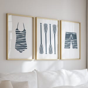 May include: A white sectional sofa with a white armchair and a wooden coffee table in a living room with white walls and sheer curtains. The coffee table has two tiers and a decorative coral piece on the top tier. There are three framed prints on the wall above the sofa, featuring a swimsuit, oars, and swim trunks.