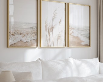 Puede incluir: Una sala de estar con un sofá blanco, dos sillas redondeadas blancas y dos mesas de centro redondas de madera. Tres cuadros con marcos dorados que muestran escenas de playa y hierba de la pampa cuelgan en la pared. Una alfombra redonda de yute está en el suelo.