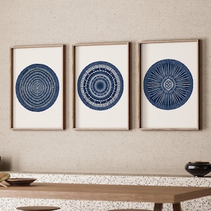 May include: A set of three rectangular wall art prints in wooden frames, each featuring a distinct dark blue circular mandala-style pattern with intricate white line details centered on a plain off-white background, displayed in a horizontal row.