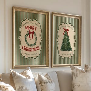 May include: Two framed Christmas art prints hang above a cream-colored sofa. The prints feature a green and white striped background with gold frames. One print says "Merry Christmas" with a wreath, the other shows a Christmas tree.