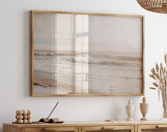 Puede incluir: Una impresión enmarcada de una escena de playa con un marco de madera marrón claro. La habitación cuenta con un aparador de madera marrón claro con puertas de caña tejida, una mesa de comedor y una lámpara tejida. También se ven jarrones decorativos y un jarrón de cristal con ramas.