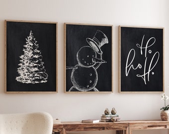 May include: Three black framed prints with white illustrations on a white wall. The prints feature a Christmas tree, a snowman, and the text "Ho Ho Ho".