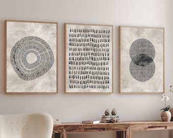 May include: Three black and white abstract art prints with geometric shapes and patterns. The prints are framed in natural wood and hung on a white wall above a wooden table and a white armchair.