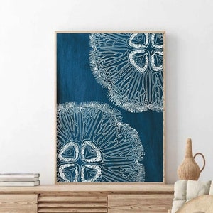 Puede incluir: Una impresi&oacute;n enmarcada con fondo azul y dos ilustraciones estilizadas blancas de un erizo de mar. La impresi&oacute;n est&aacute; colgada en una pared blanca sobre un armario de madera.