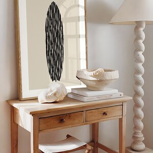 Puede incluir: Una impresi&oacute;n enmarcada con un dise&ntilde;o abstracto en blanco y negro de una tabla de surf sobre un fondo beige. La impresi&oacute;n est&aacute; colgada en una pared sobre una mesa de madera con dos cajones. Un cuenco de cer&aacute;mica blanco y una escultura blanca est&aacute;n sobre la mesa.