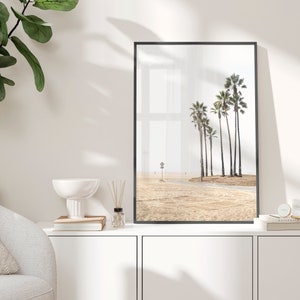 May include: A black framed print of a beach scene with palm trees and a sandy beach.