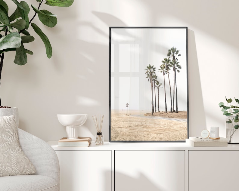 May include: A black framed print of a beach scene with palm trees and a sandy beach.