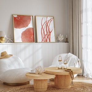 May include: Two framed illustrations of coral and seaweed in a living room setting with a white couch, two coffee tables, and a lamp. The illustrations are in shades of red and white.