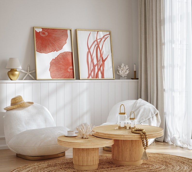 May include: Two framed illustrations of coral and seaweed in a living room setting with a white couch, two coffee tables, and a lamp. The illustrations are in shades of red and white.