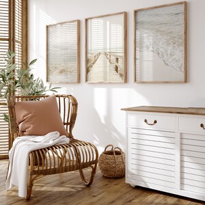 May include: A white cabinet with two doors and a drawer, featuring a wood top and a woven basket. The cabinet is in a room with a wicker chair, a throw blanket, and three framed beach-themed prints.