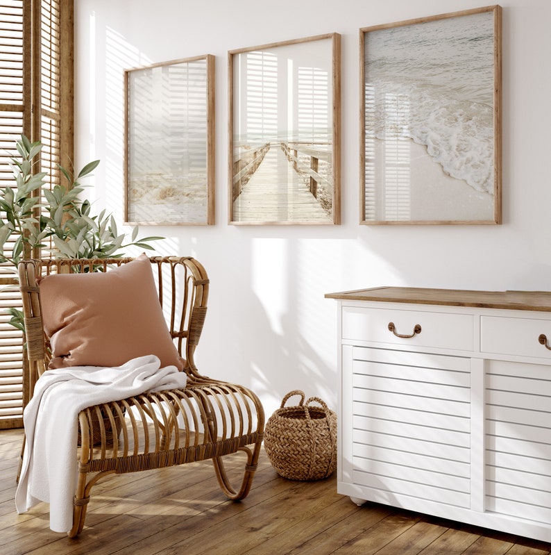 May include: A white cabinet with two doors and a drawer, featuring a wood top and a woven basket. The cabinet is in a room with a wicker chair, a throw blanket, and three framed beach-themed prints.