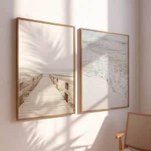 May include: Two framed photographs of beach scenes. The first photo shows a wooden walkway leading to the ocean with a palm tree shadow in the background. The second photo shows a close-up of a wave breaking on a sandy beach.