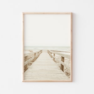 May include: A wooden boardwalk leads to the ocean, with a light brown wooden railing on either side. The ocean is a light blue color, and the sky is a light gray color.