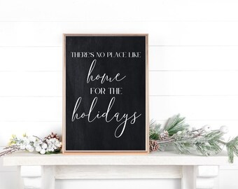 May include: Black framed sign with white text that reads "There's no place like home for the holidays". The sign is sitting on a white mantel with a sprig of frosted pine branches.