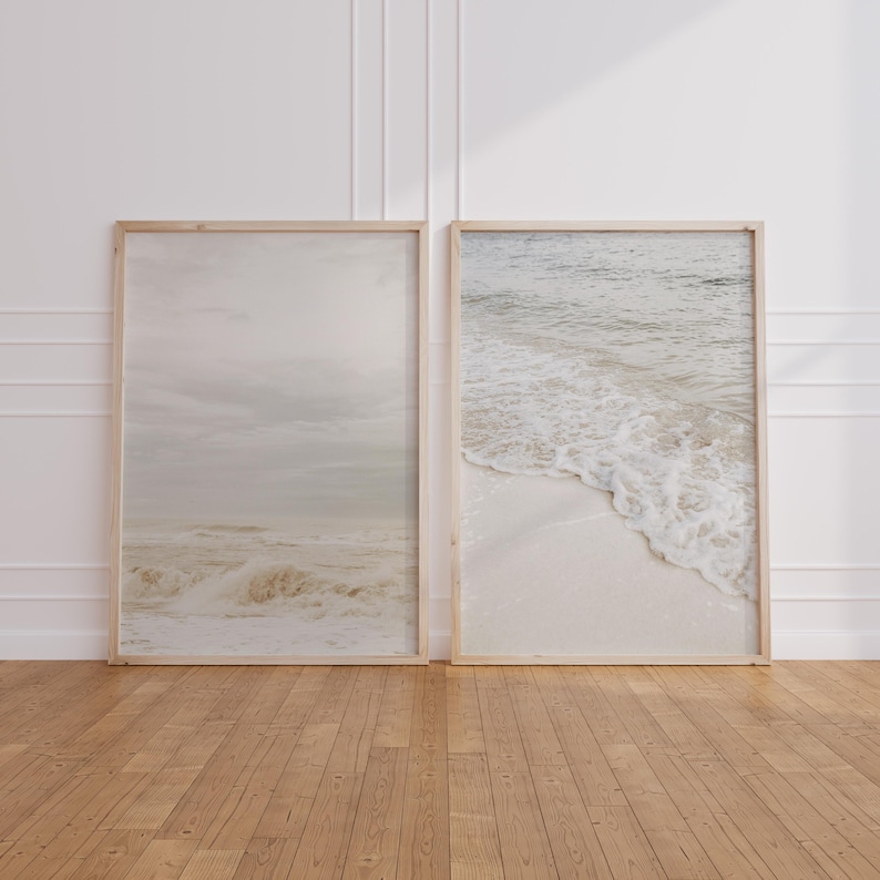 May include: Two framed photographs of ocean waves crashing on a sandy beach. The photos are in a light wood frame and are hanging on a white wall.