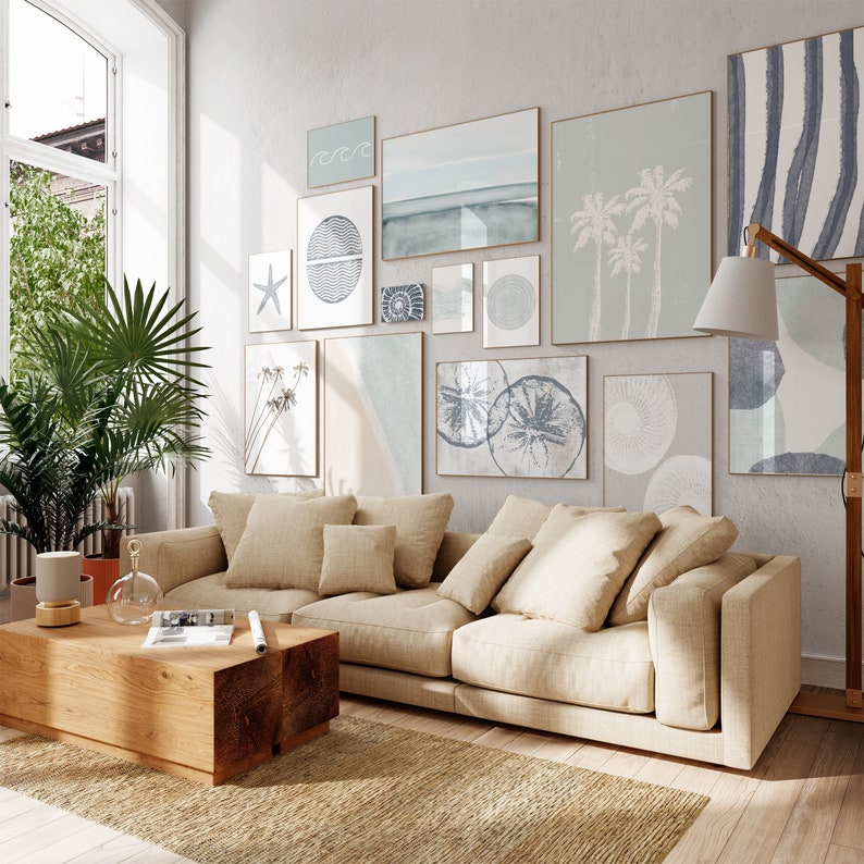 May include: A light beige sectional sofa with multiple pillows in a living room with a gallery wall of abstract art prints in shades of blue and gray. The art prints feature geometric shapes, waves, and starfish.