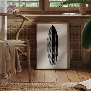 Puede incluir: Una impresi&oacute;n abstracta en blanco y negro de una tabla de surf colgada en un marco de madera en una pared. El marco est&aacute; en una pared con un panel de rat&aacute;n tejido y una silla de madera con una manta de lana marr&oacute;n.