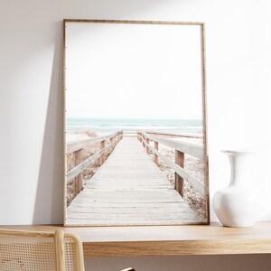 May include: A framed photograph of a wooden boardwalk leading to a beach with blue water and white sand.