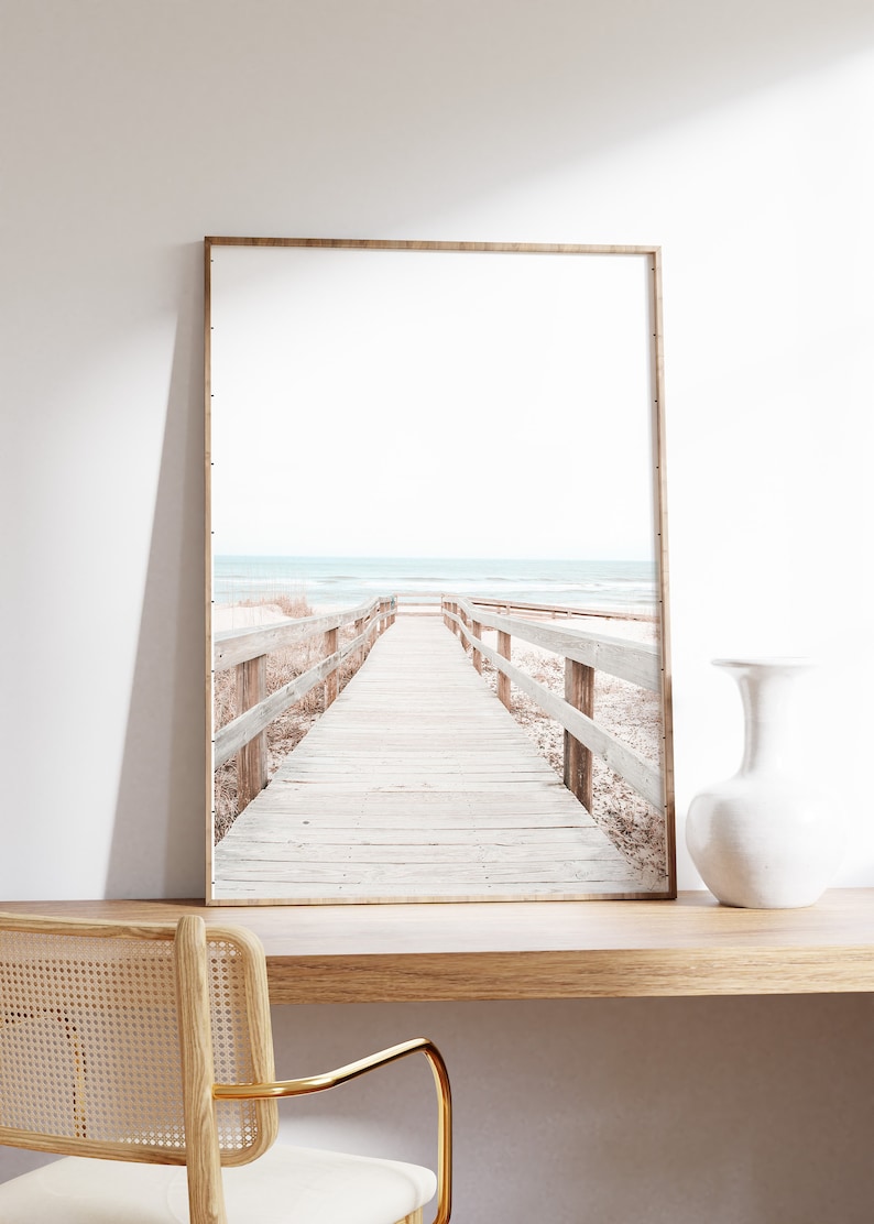 May include: A framed photograph of a wooden boardwalk leading to a beach with blue water and white sand.