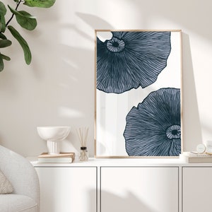 Op de afbeelding: Een ingelijst drukwerk met een witte achtergrond en twee blauwe abstracte bloemmotieven. De print is in een licht houten frame.