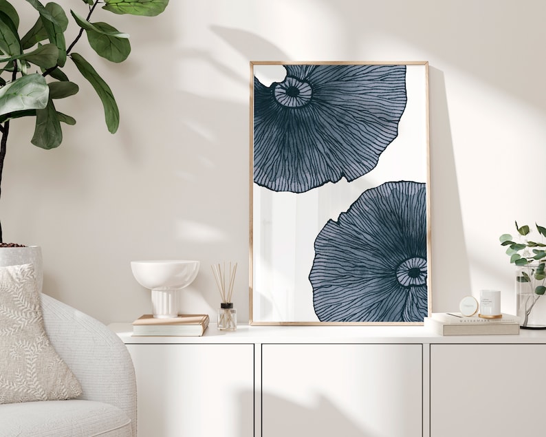 Op de afbeelding: Een ingelijst drukwerk met een witte achtergrond en twee blauwe abstracte bloemmotieven. De print is in een licht houten frame.