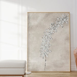 Puede incluir: Una impresi&oacute;n en lienzo beige con un dibujo en blanco y negro de una rama de flores. La impresi&oacute;n est&aacute; enmarcada en un marco dorado fino y est&aacute; colgada en una pared blanca.