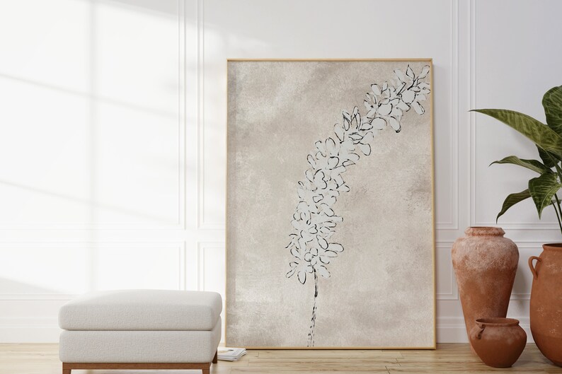 Puede incluir: Una impresi&oacute;n en lienzo beige con un dibujo en blanco y negro de una rama de flores. La impresi&oacute;n est&aacute; enmarcada en un marco dorado fino y est&aacute; colgada en una pared blanca.