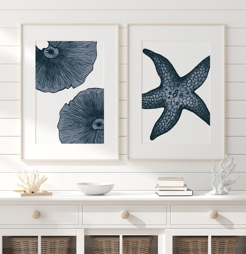Op de afbeelding: Twee ingelijste prints met een nautisch thema. De linker print toont twee gestileerde illustraties van zeeanemonen in blauw en wit. De rechter print toont een gestileerde illustratie van een zeester in blauw en wit.