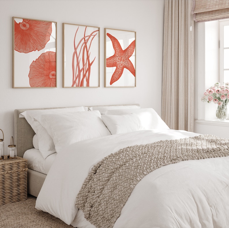 May include: A white bed with a beige knitted throw blanket and three framed prints of coral, seaweed, and a starfish in shades of orange and white.