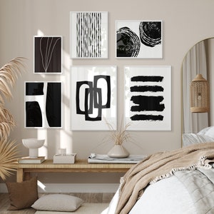 May include: A bedroom interior with a bed, a nightstand, and a wall decorated with black and white abstract art prints. The prints are framed and hung in a grid pattern. The room is decorated in a minimalist style with a neutral color palette.