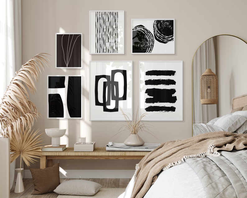 May include: A bedroom interior with a bed, a nightstand, and a wall decorated with black and white abstract art prints. The prints are framed and hung in a grid pattern. The room is decorated in a minimalist style with a neutral color palette.