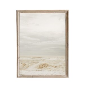 Puede incluir: Una fotograf&iacute;a enmarcada de un paisaje mar&iacute;timo con olas blancas rompiendo en la costa. El cielo es de un azul claro con nubes blancas. El marco es de madera marr&oacute;n claro.