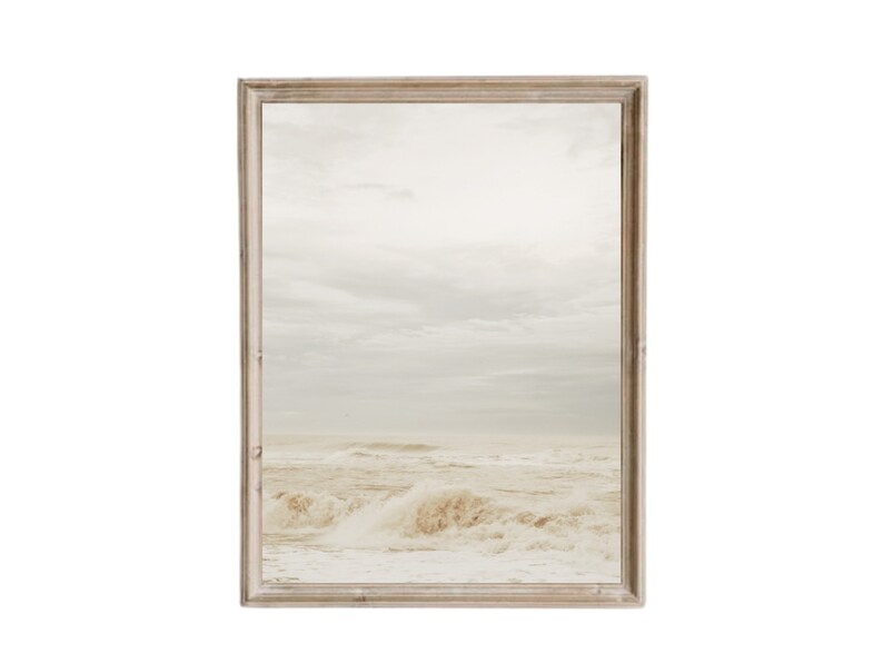 Puede incluir: Una fotograf&iacute;a enmarcada de un paisaje mar&iacute;timo con olas blancas rompiendo en la costa. El cielo es de un azul claro con nubes blancas. El marco es de madera marr&oacute;n claro.