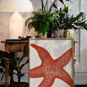 May include: A framed print of a red starfish on a white background. The print is displayed on a wooden table with plants in pots.