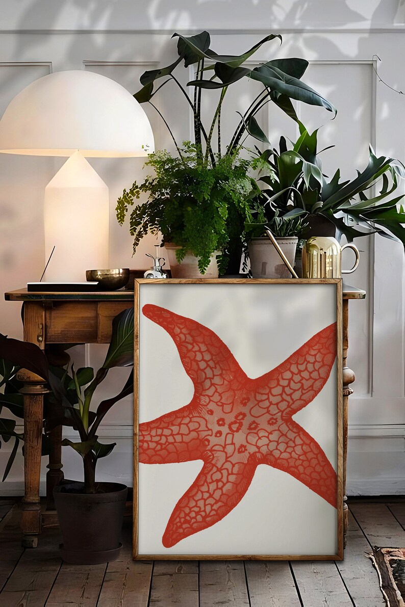 May include: A framed print of a red starfish on a white background. The print is displayed on a wooden table with plants in pots.