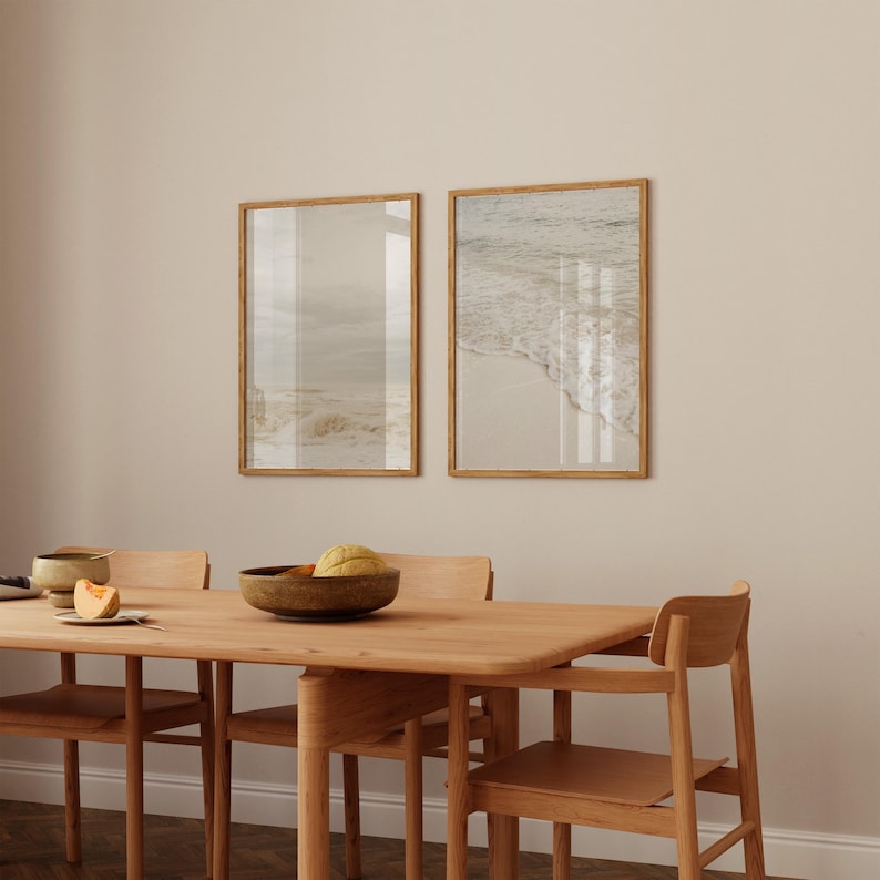 May include: A wooden dining table with four chairs, set with a bowl of fruit and a plate with a slice of melon. Two framed photographs of a beach scene hang on the wall behind the table.
