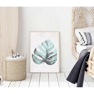 May include: A framed print of a single, large, teal green monstera leaf on a white background.