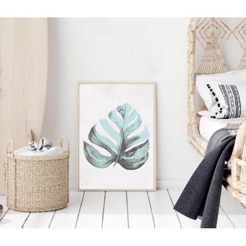 May include: A framed print of a single, large, teal green monstera leaf on a white background.