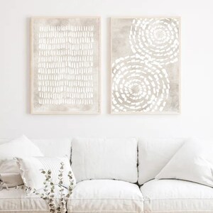 Puede incluir: Dos impresiones de arte abstracto enmarcadas con un esquema de color blanco y gris. La impresi&oacute;n de la izquierda presenta un patr&oacute;n de l&iacute;neas blancas sobre un fondo gris. La impresi&oacute;n de la derecha presenta dos patrones circulares blancos sobre un fondo gris.