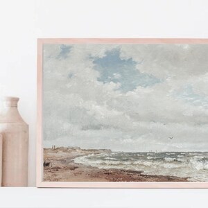 Puede incluir: Una pintura enmarcada que representa un paisaje mar&iacute;timo con un cielo nublado, una playa de arena y un oc&eacute;ano agitado con olas. La pintura est&aacute; en un marco de madera claro.