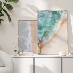 May include: Two framed photographs of ocean waves crashing on a sandy beach. The top photo is a close-up of the waves, while the bottom photo shows a wider view of the beach.