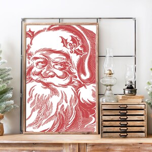 K&ouml;nnte beinhalten: Eine rote und wei&szlig;e Vintage-Illustration von Santa Claus' Gesicht. Die Illustration ist gerahmt und h&auml;ngt an einer Wand.