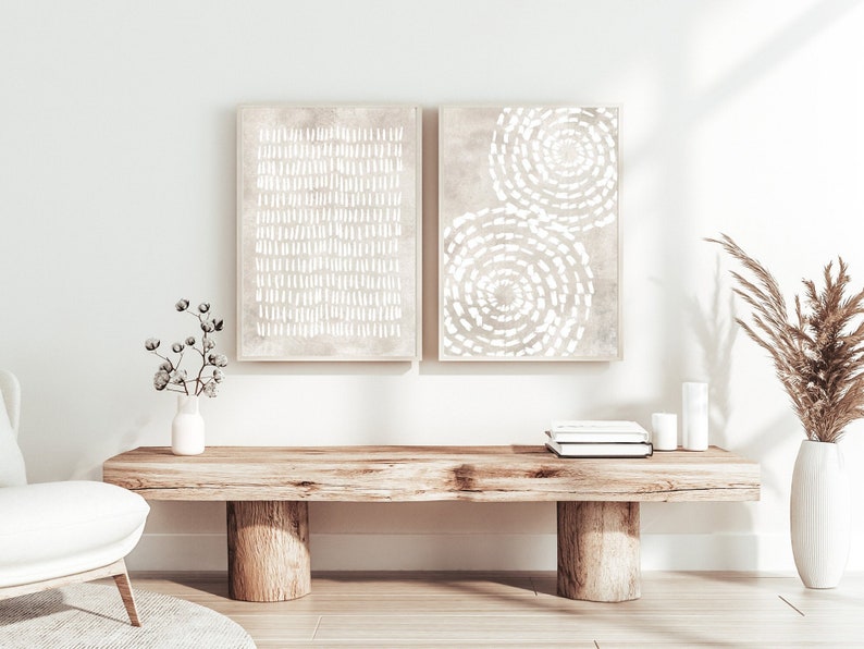 Puede incluir: Dos impresiones de arte abstracto con dise&ntilde;os geom&eacute;tricos blancos sobre un fondo beige. Las impresiones est&aacute;n enmarcadas y colgadas en una pared blanca sobre un banco de madera con un jarr&oacute;n de flores secas y velas.
